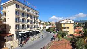 A multi-story hotel with balconies, flags, and a street view. - Piccolo Hotel (Diano Marina)