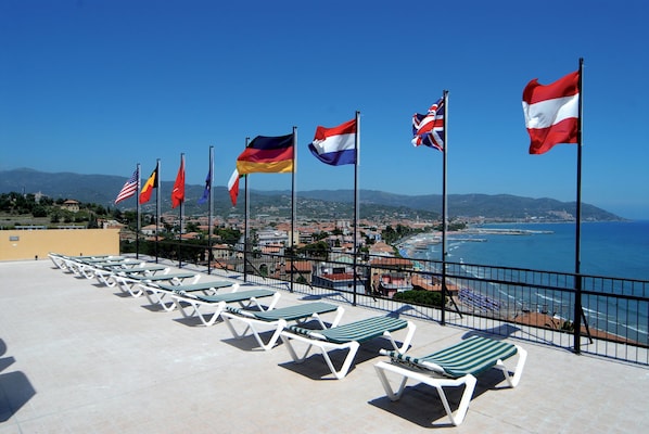 Une terrasse sur le toit, dotée de chaises longues et ornée de drapeaux de différents pays, offrant une vue panoramique sur le paysage urbain côtier.