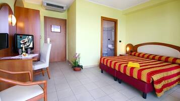 A hotel room with a bed, a desk with a chair, a television, and a potted plant.