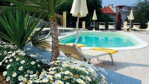 A swimming pool with lounge chairs and umbrellas, surrounded by palm trees and daisies. - Piccolo Hotel (Diano Marina)