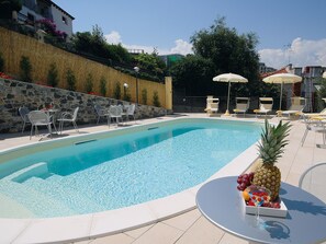 Une piscine entourée d’un mur de pierre et de verdure, avec des chaises longues et des parasols.