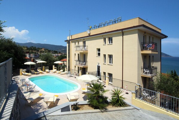 A hotel with a swimming pool, outdoor seating, and balconies with views of the sea.