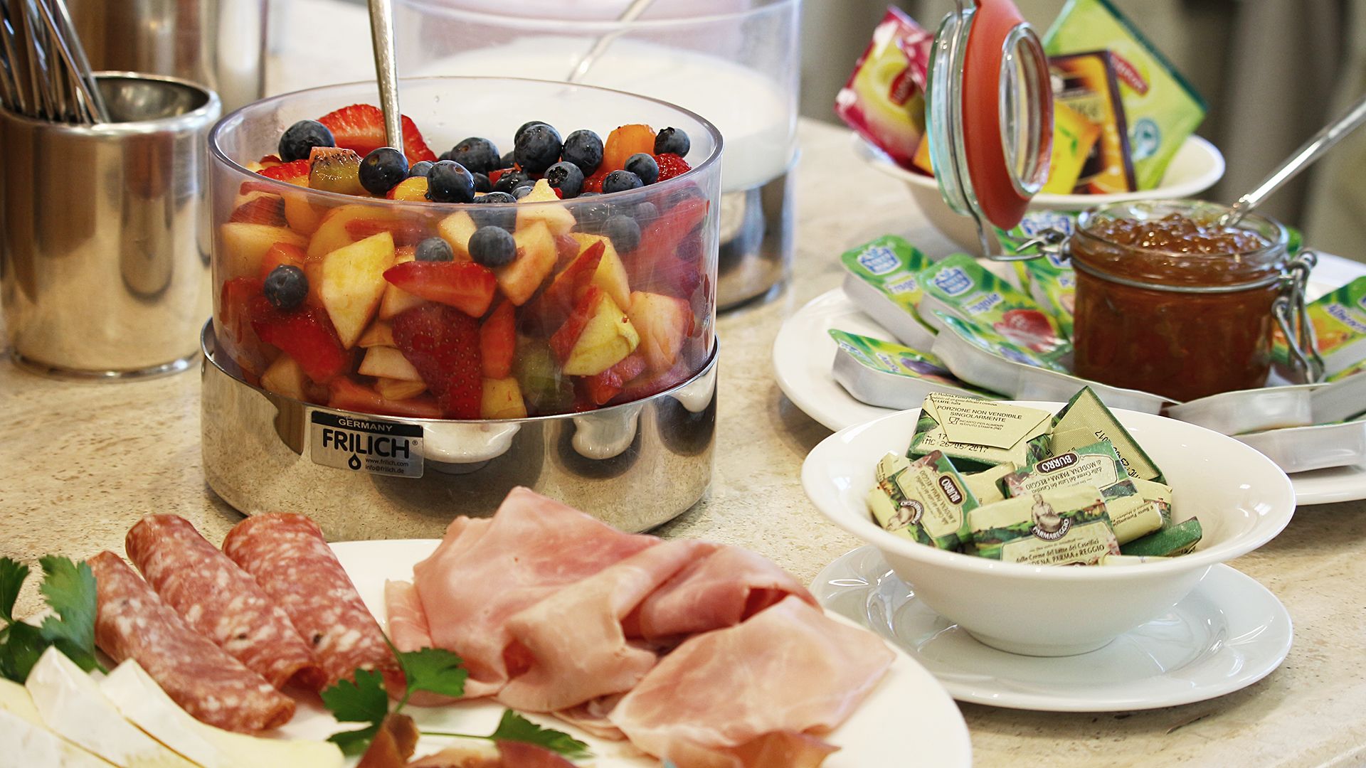 A buffet with a variety of food items including a fruit salad, cheese, and meats.
