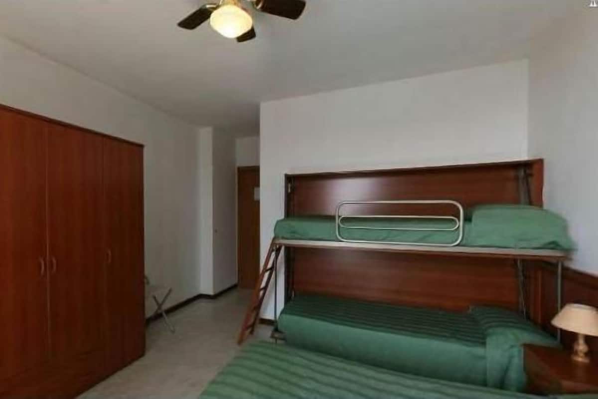 Una stanza con un letto a castello, un armadio in legno e una ventola a soffitto.