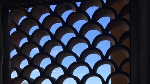 Une fenêtre ornée d’un motif géométrique, d’où l’on peut admirer la mer et les bâtiments.