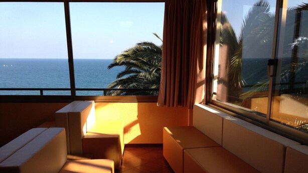 Une chambre avec vue sur l’océan, comprenant un coin salon avec un canapé et un banc, ainsi qu’une grande fenêtre avec des rideaux.