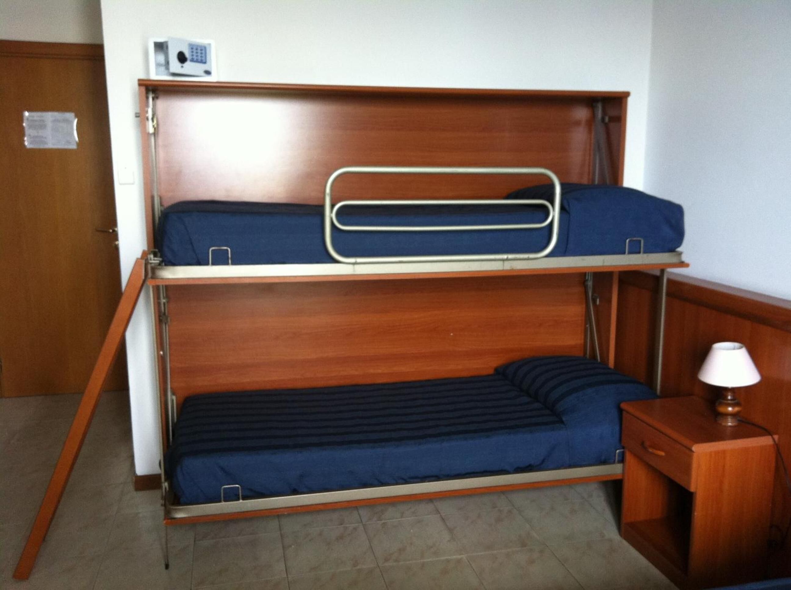 A bunk bed with a desk and lamp, wooden walls, and a door.