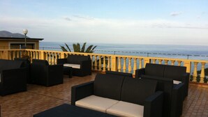 Une terrasse dotée de meubles en osier, une vue sur la mer et une balustrade jaune.