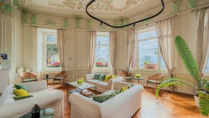 Ein geräumiges Wohnzimmer mit einem weißen Sofa, grünen und gelben Kissen, einem Couchtisch und einer großen Kübelpflanze.