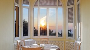 Ein Essbereich mit Tisch für zwei Personen, großen Fenstern mit Sonnenuntergangsblick und einer Netzstruktur an den Wänden.