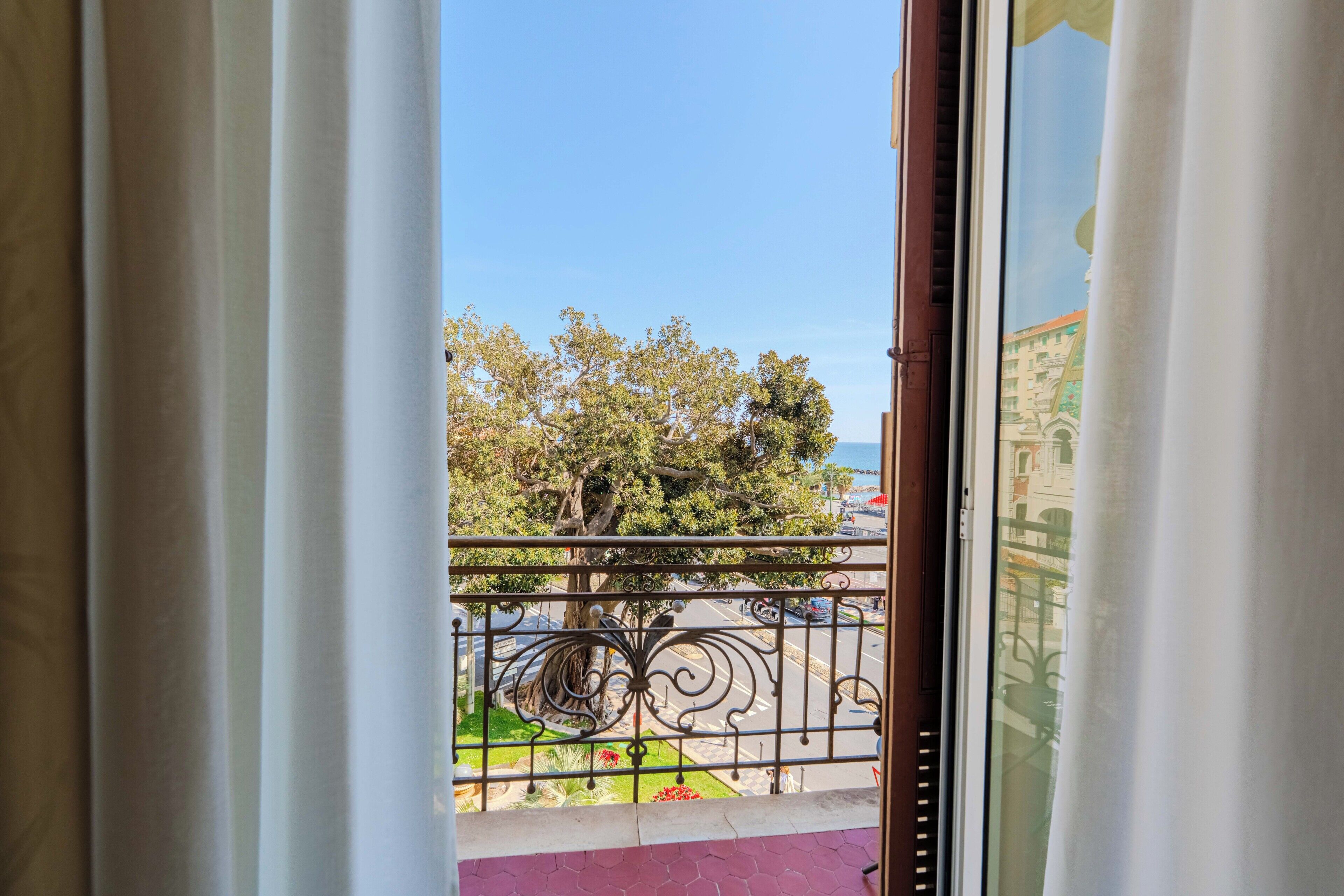 A balcony with a metal railing, a view of trees, and a building in the background.