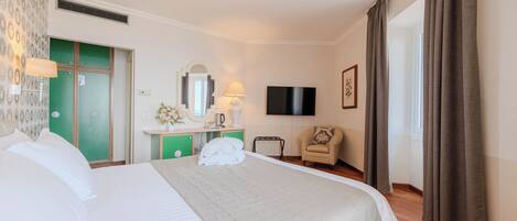 Una habitación de hotel con cama, tocador con espejo, televisión, silla y ventana con cortinas.