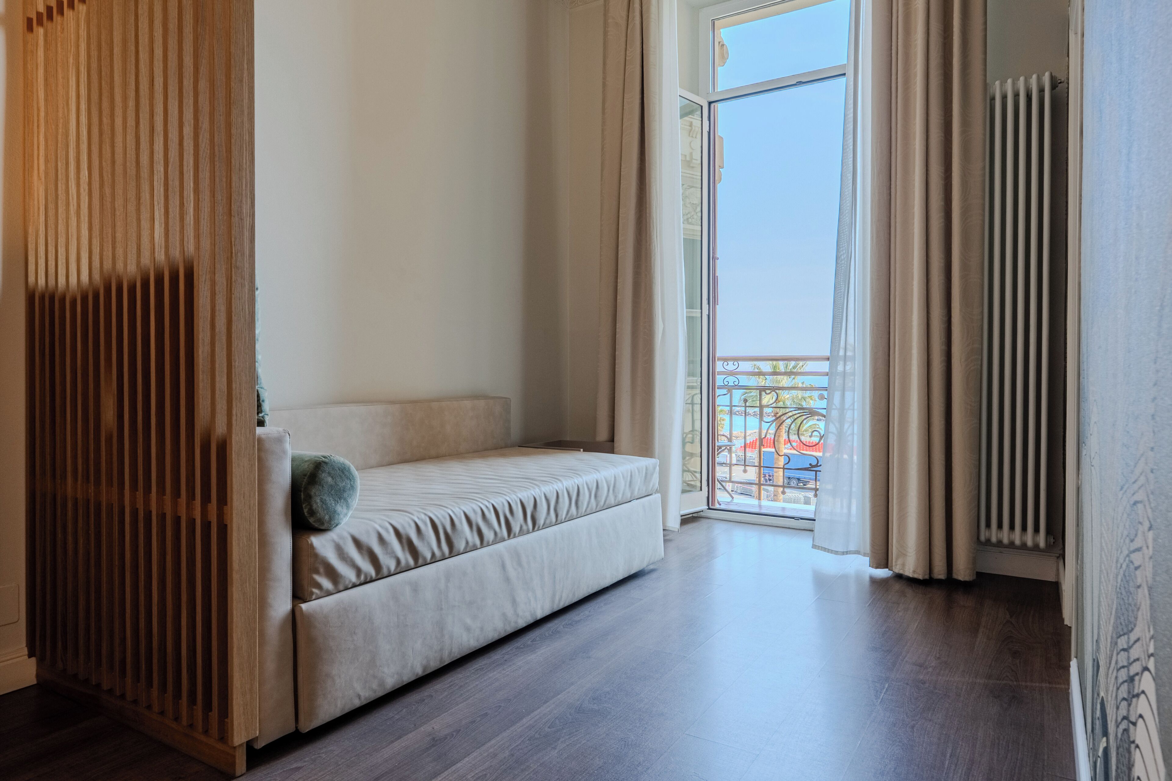 A room with a sofa, a wooden partition, a radiator, and a view of a balcony.