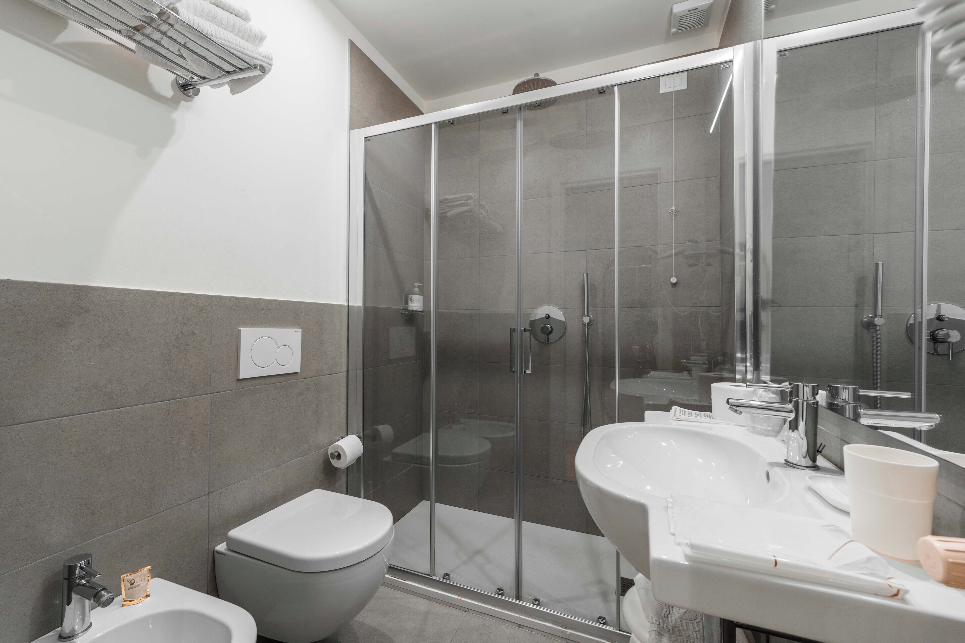 A modern bathroom with a glass-enclosed shower, a bidet, a sink, and a toilet.
