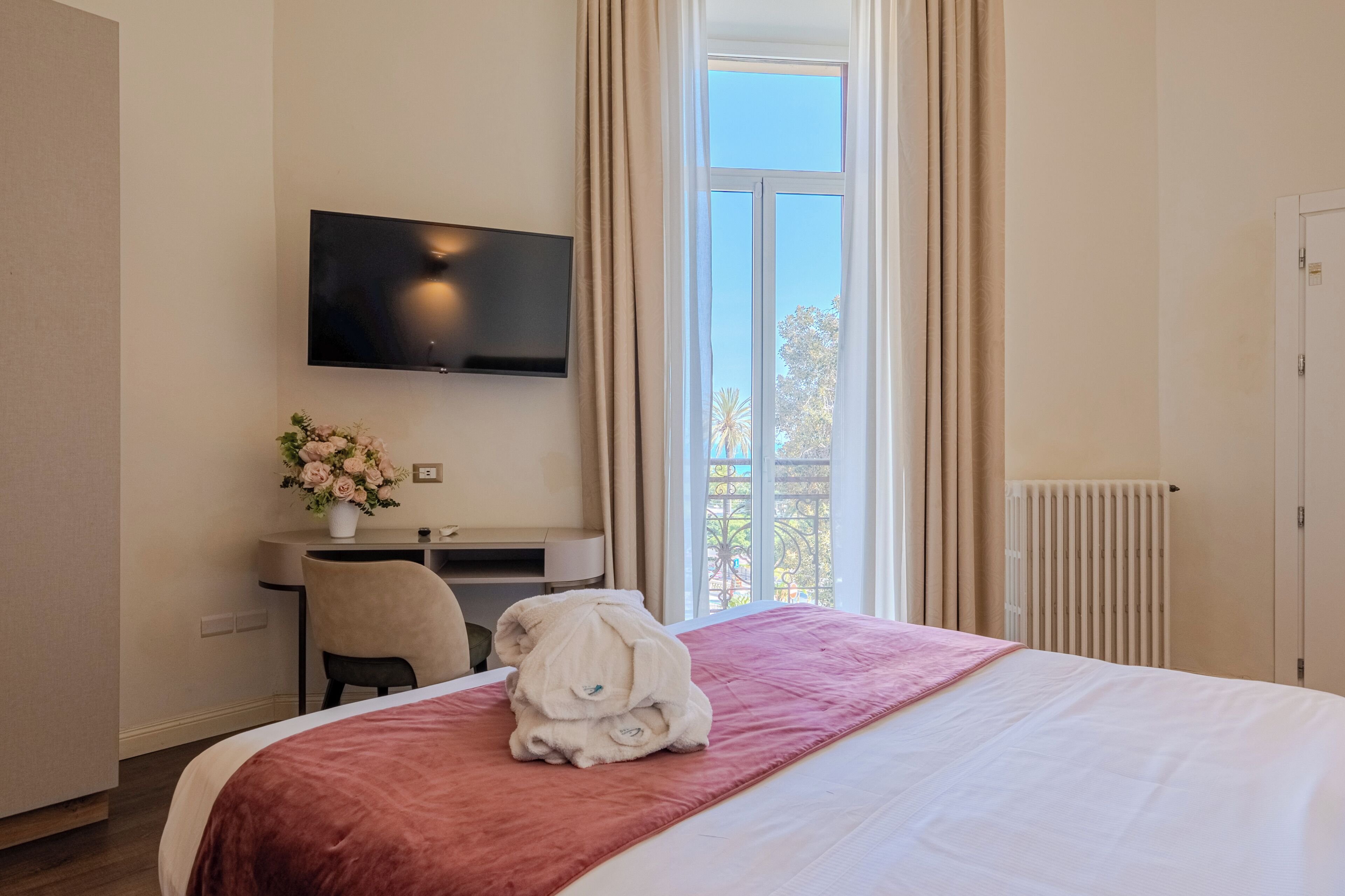 A hotel room with a bed, a desk, a TV, and a window with curtains.
