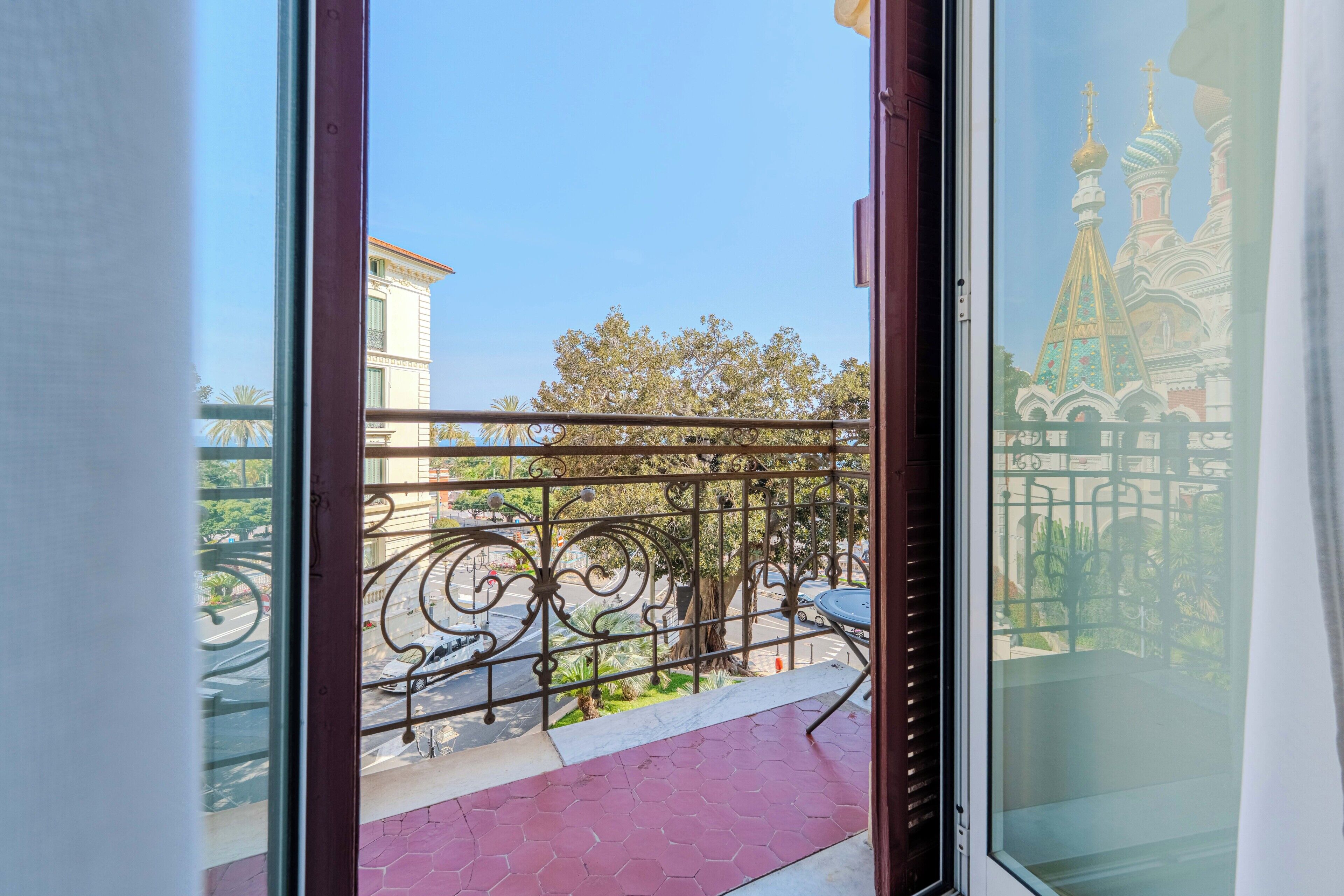 A balcony with a wrought iron railing, a red-tiled floor, and a view of a building with distinctive domes.