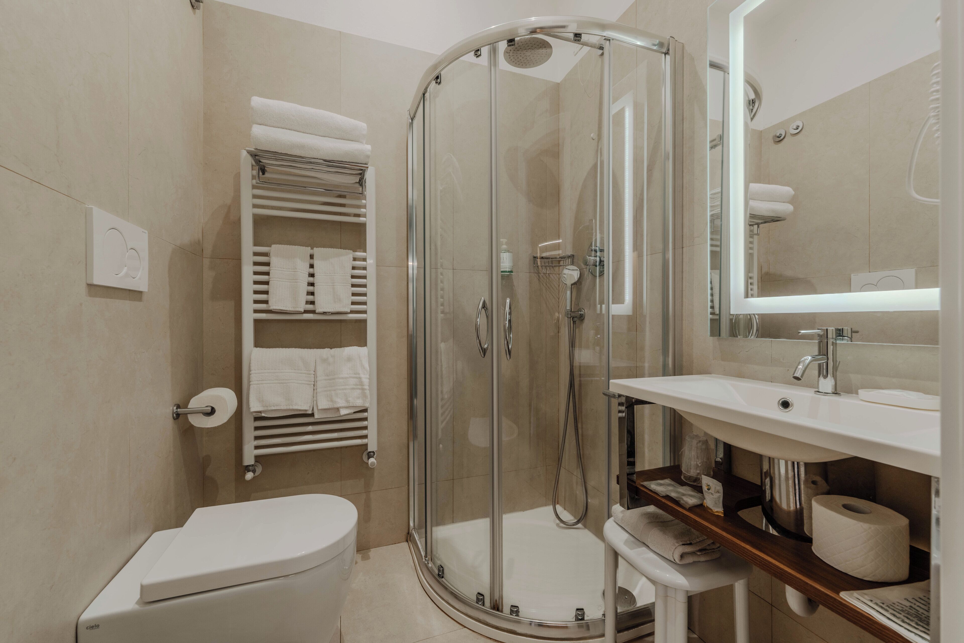A modern bathroom with a glass-enclosed shower, a toilet, a sink with a mirror, and a towel rack with neatly folded towels.