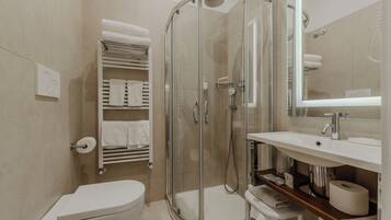 A modern bathroom with a glass-enclosed shower, a toilet, a sink with a mirror, and a towel rack with neatly folded towels.