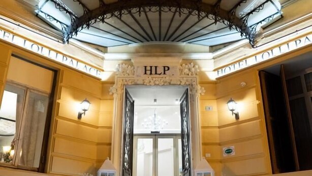 Ein imposanter Eingangsbereich mit einer Treppe, die zu einem Balkon führt, gekennzeichnet mit den Schildern „HLP“ und „HOTEL LOLLIPALACE“.