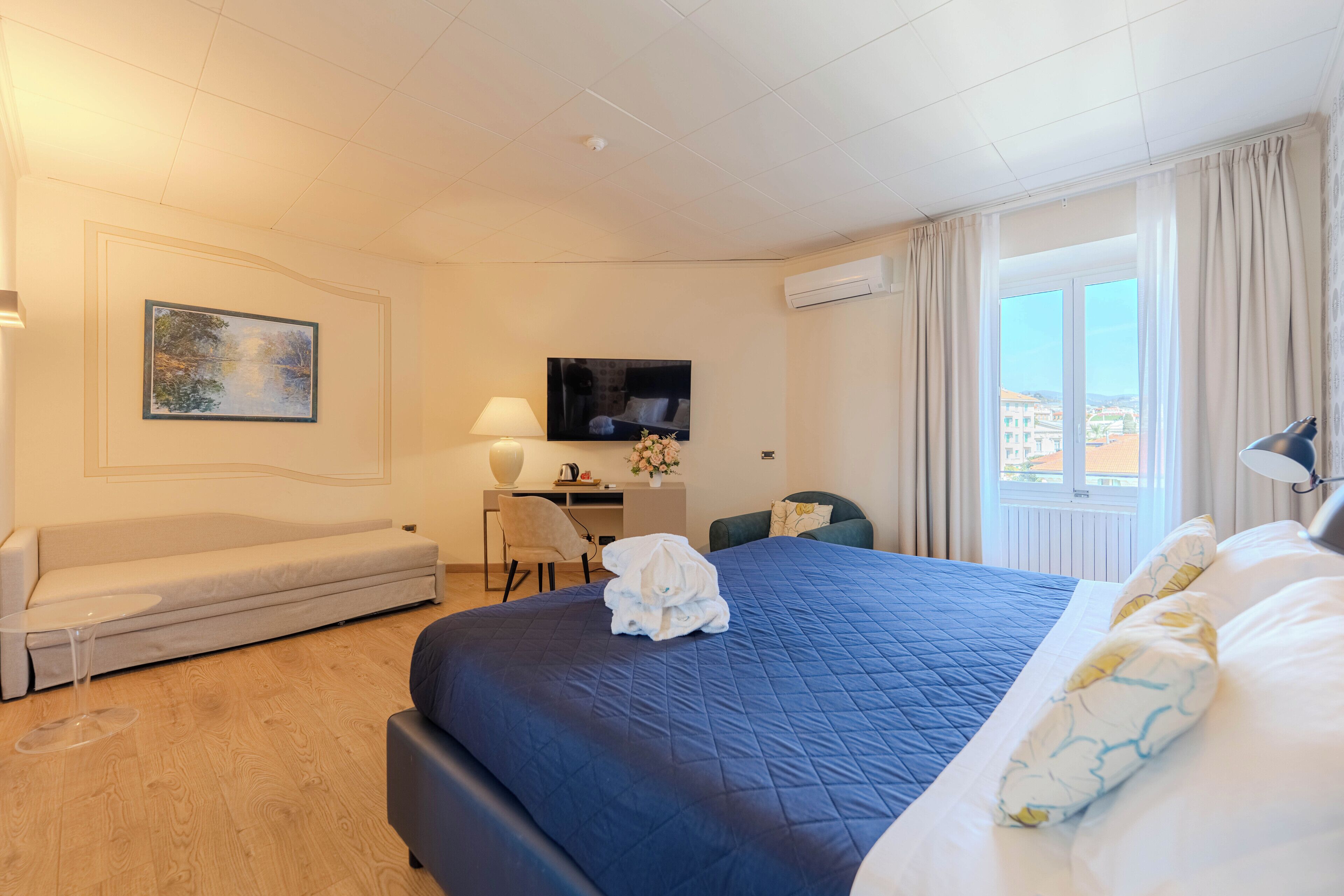 Habitación de hotel con una cama grande, un sofá, un escritorio, un televisor y una ventana con cortinas.
