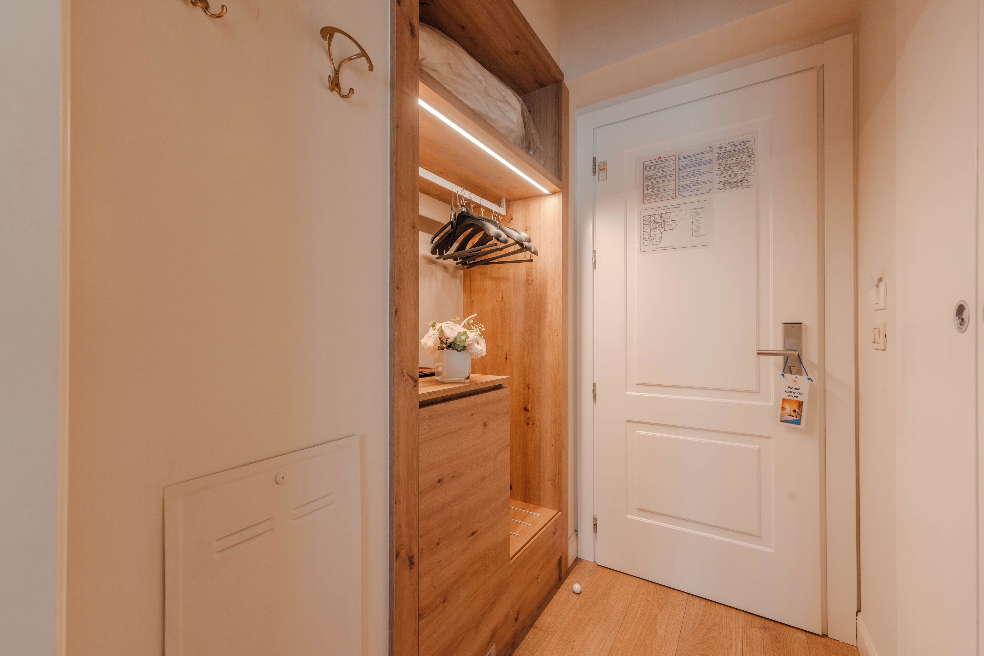 A hallway with a wooden wardrobe, a hanging coat rack, a small table with a vase, and a white door with a notice on it.