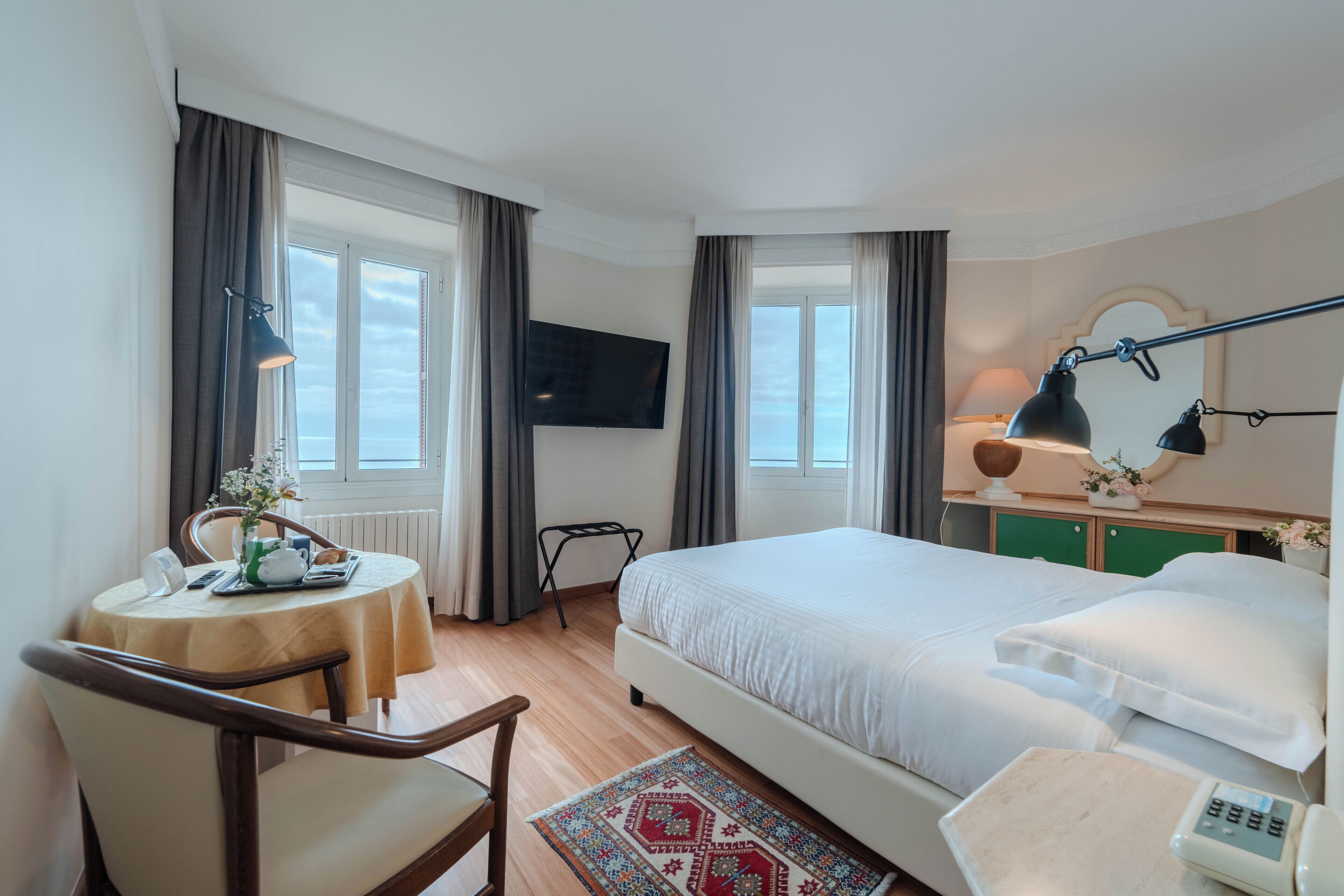 A hotel room with a bed, a desk with a chair, a TV, and a bedside table with a lamp.