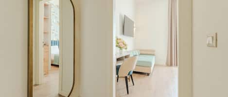 A room with a large mirror, a bed, a desk with a chair, a TV, and a window with curtains.