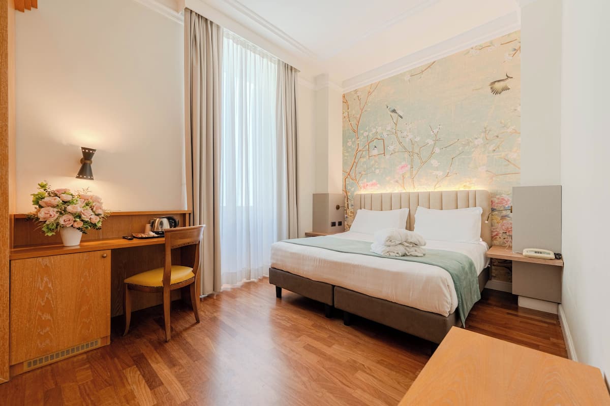 Una habitación de hotel con cama, escritorio, silla y un mural floral en la pared.