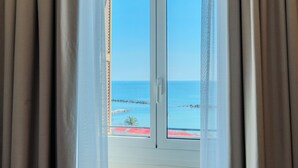 Blick durch ein Fenster mit Vorhängen, zeigt einen klaren Himmel und eine entfernte Küstenlinie.