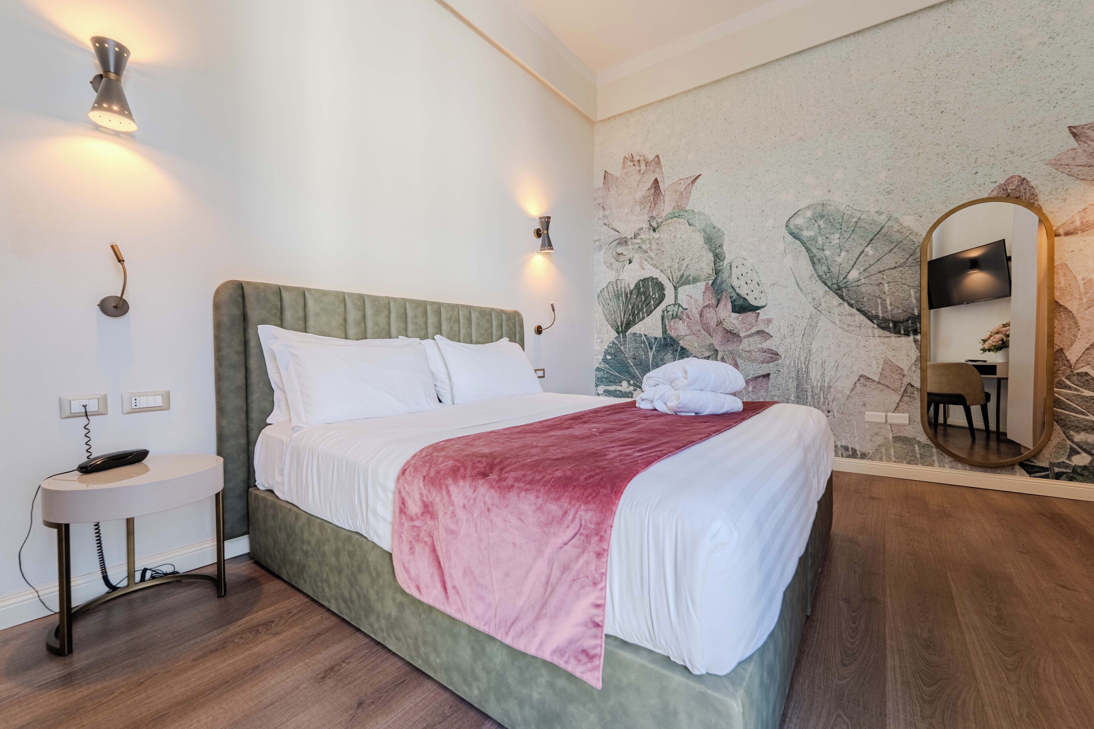 Ein ordentlich gemachtes Bett mit grünem Kopfteil, einer roten Decke und einem an der Wand befestigten Spiegel.