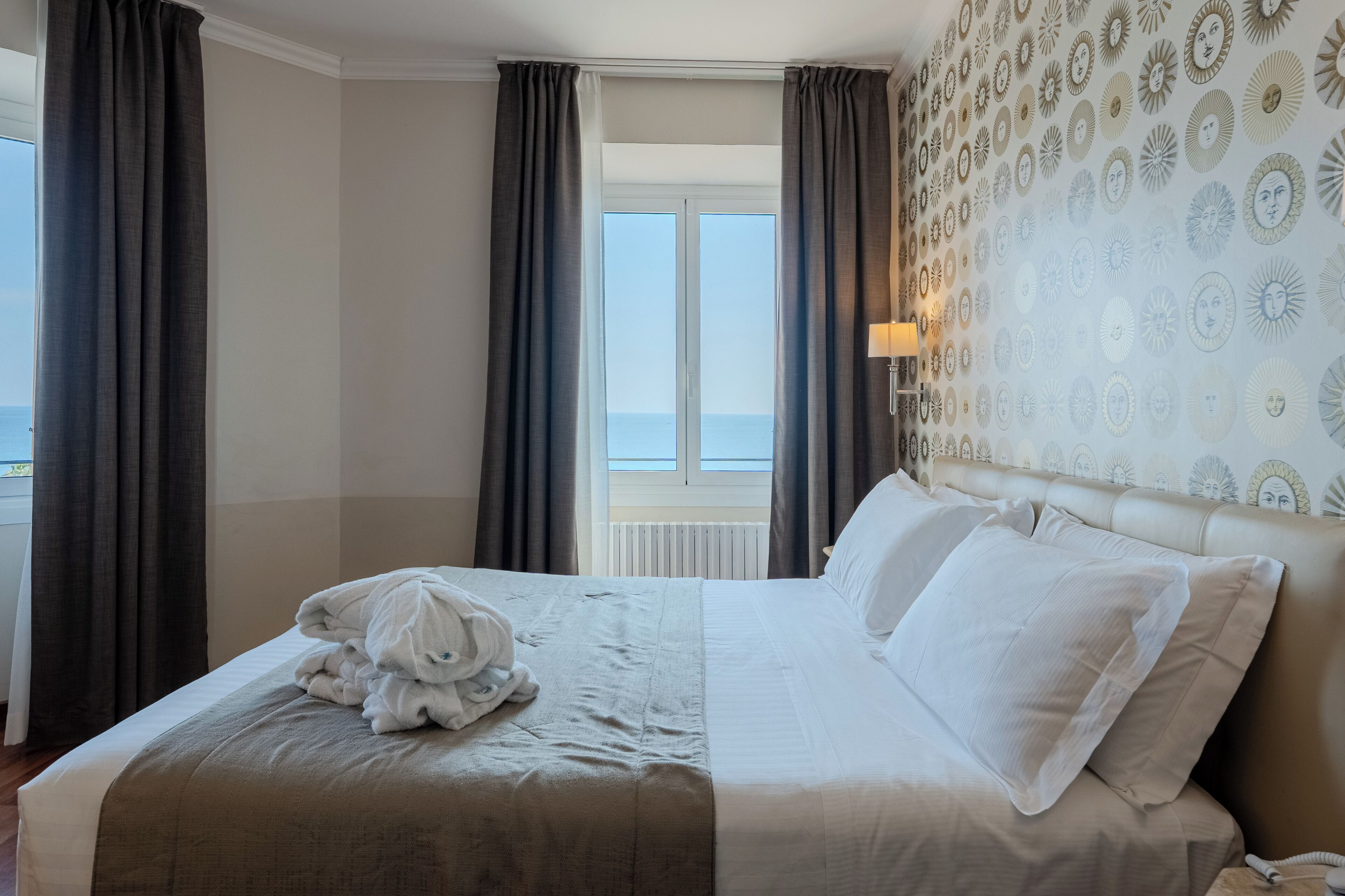 Habitación de hotel con cama, cortinas, ventana con vistas y pared estampada.