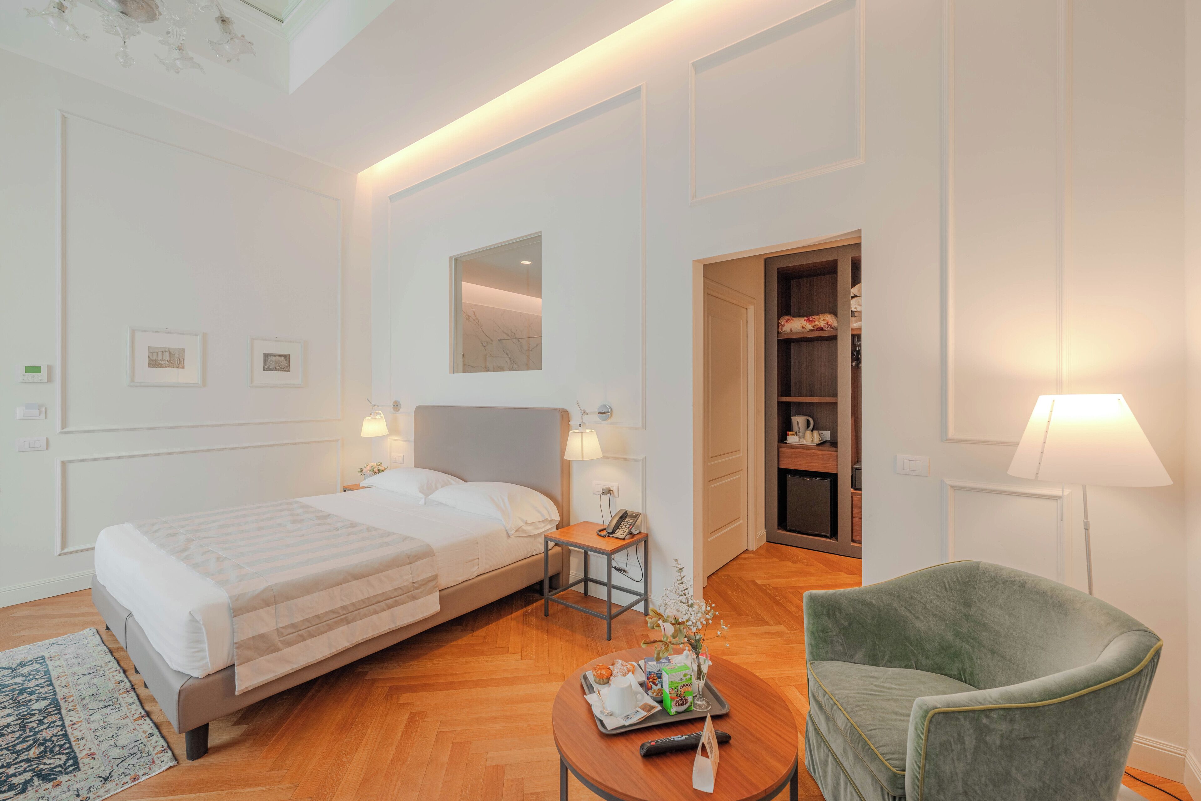 Une chambre d’hôtel comprenant un lit, une table de chevet, une lampe, un fauteuil et une petite table avec un plateau.