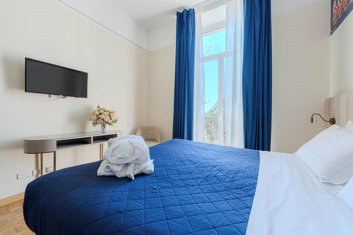 Habitación de hotel con cama, televisor de pantalla plana, escritorio y ventana con cortinas.