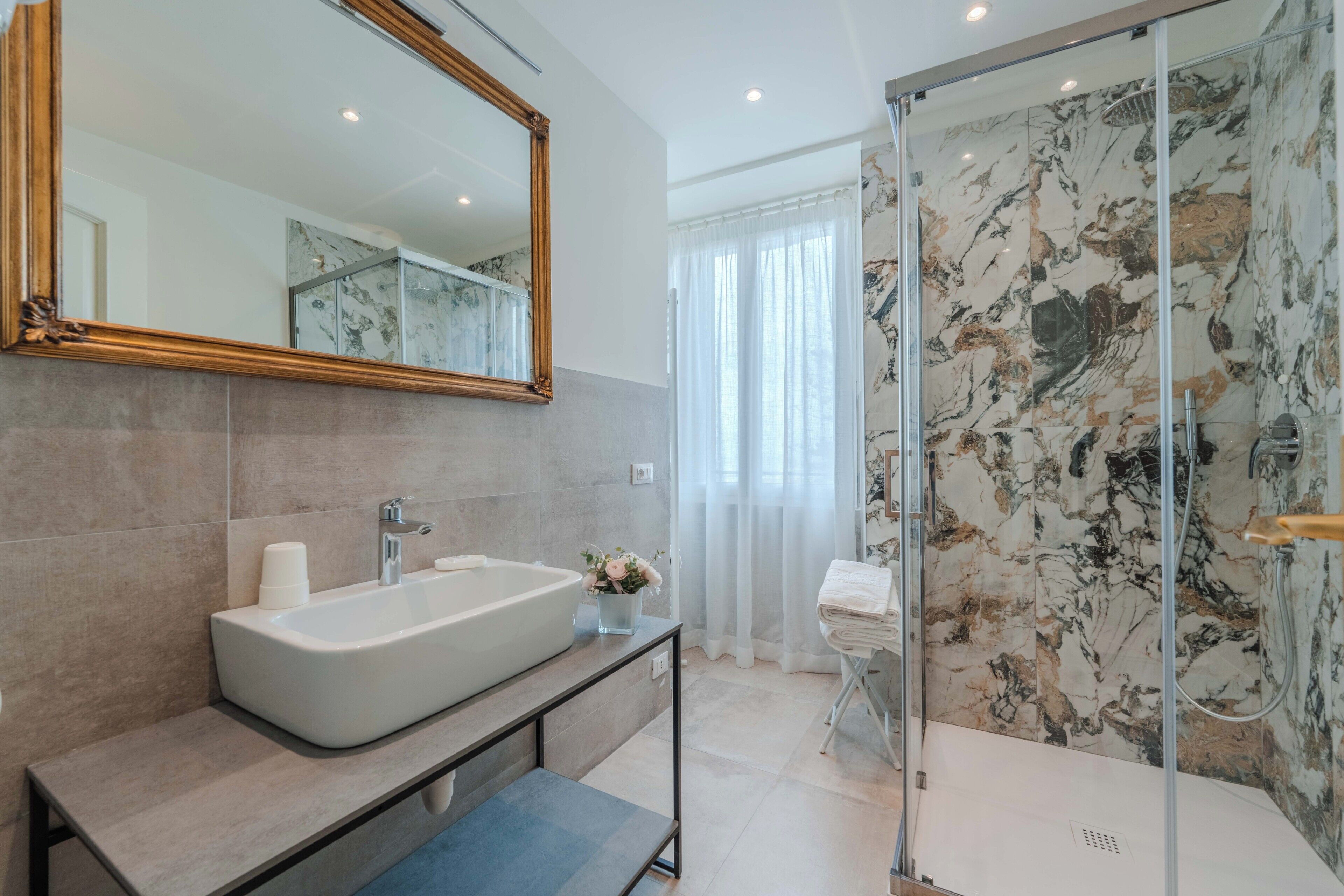 Un baño moderno con un espejo grande, una bañera, una ducha y paredes de mármol.