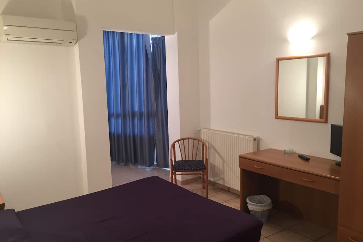 A room with a bed, a desk, a chair, a radiator, a window with curtains, and a mirror.