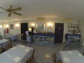 A restaurant with tables covered in patterned tablecloths, a counter with a TV, and wall-mounted lights.