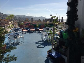 Terraza en la azotea con mobiliario exterior, plantas en macetas y vistas de la ciudad.