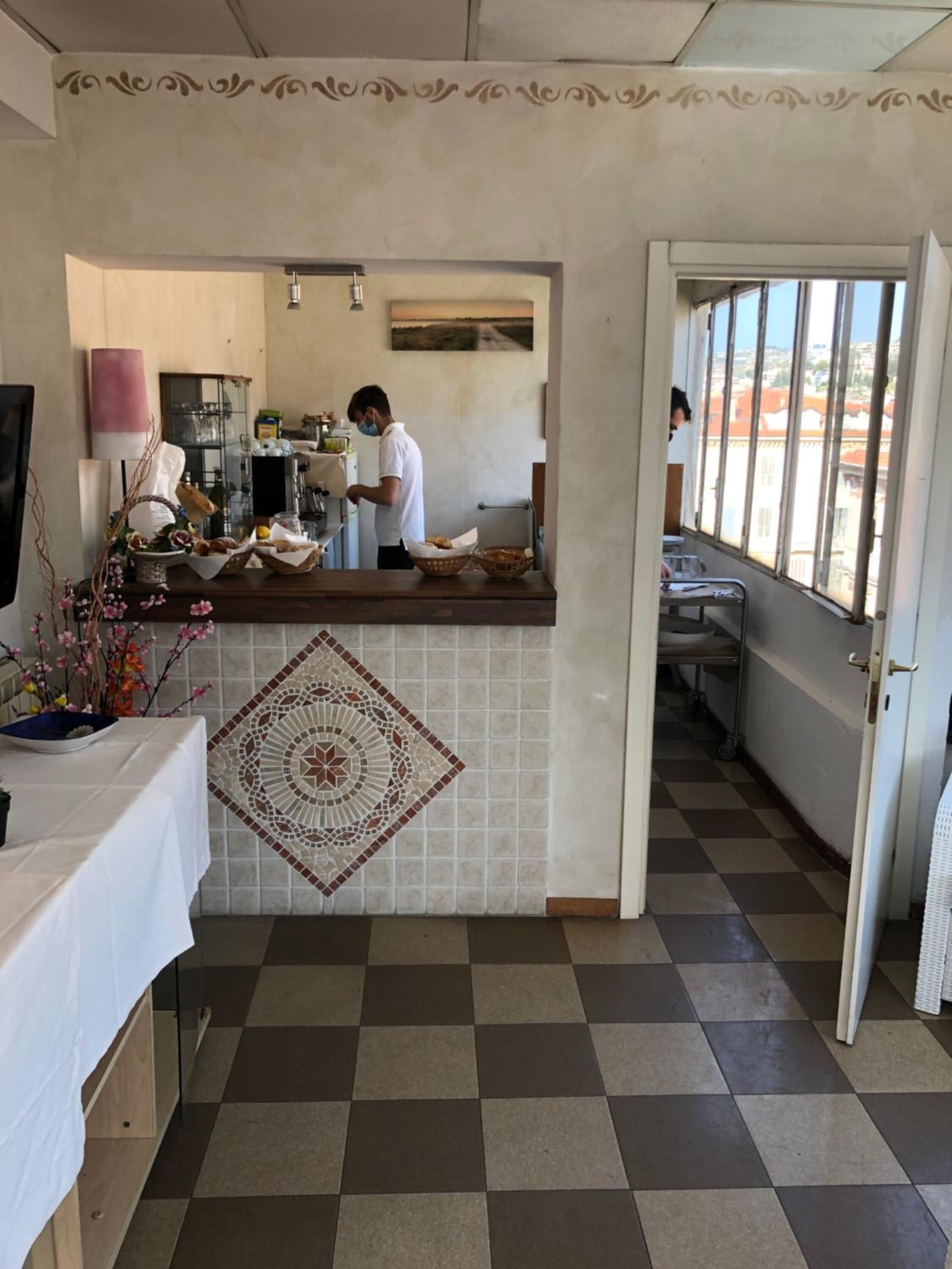 A restaurant with a checkered floor, a decorative tile wall, and a counter where a person is preparing food.
