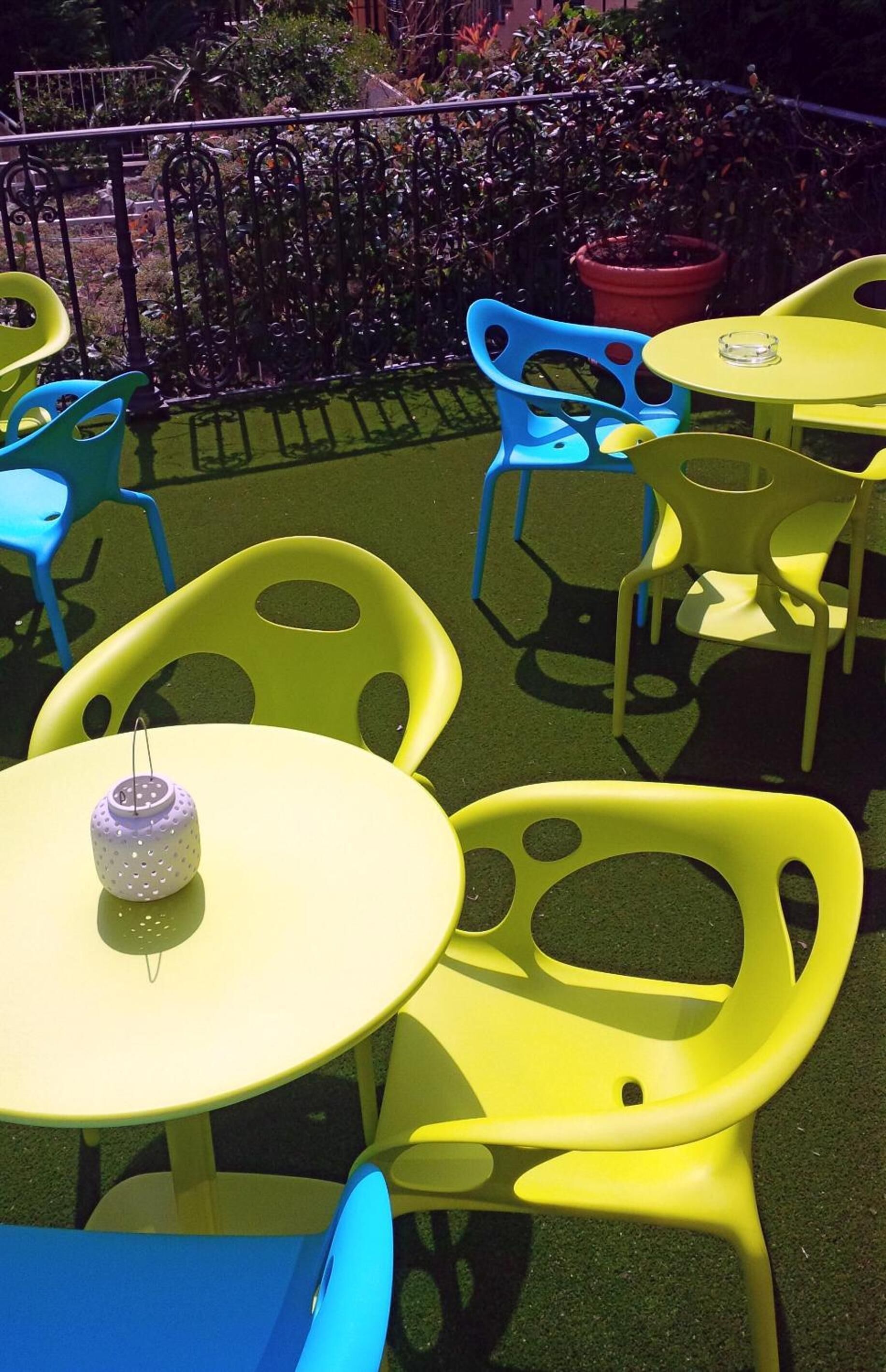 Outdoor seating with yellow and blue plastic chairs and tables, a small purple lantern, and a red planter.
