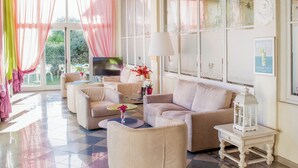 Un salón amplio con un gran sofá, una mesa de centro y un televisor. Hay ventanas grandes con cortinas, una lámpara decorativa y un cuadro en la pared.