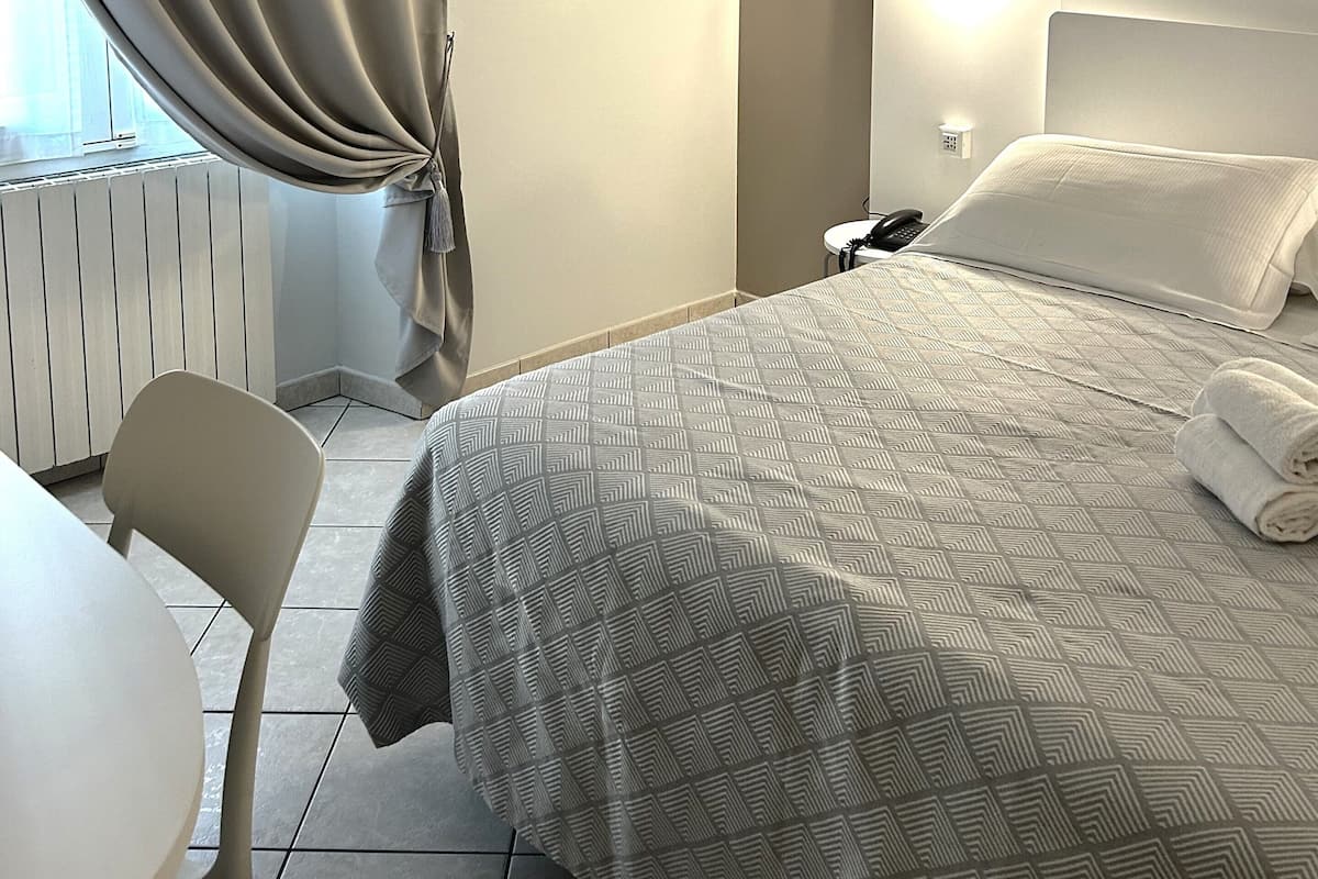 Une chambre d’hôtel avec un lit, une table de chevet, une chaise et une fenêtre avec des rideaux.
