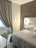 Una habitación de hotel con cama, mesita de noche, silla y ventana con cortinas.