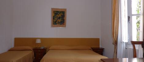 Habitación de hotel con dos camas, cabecero de madera, mesita de noche con lámpara, un cuadro en la pared y una ventana con cortinas.