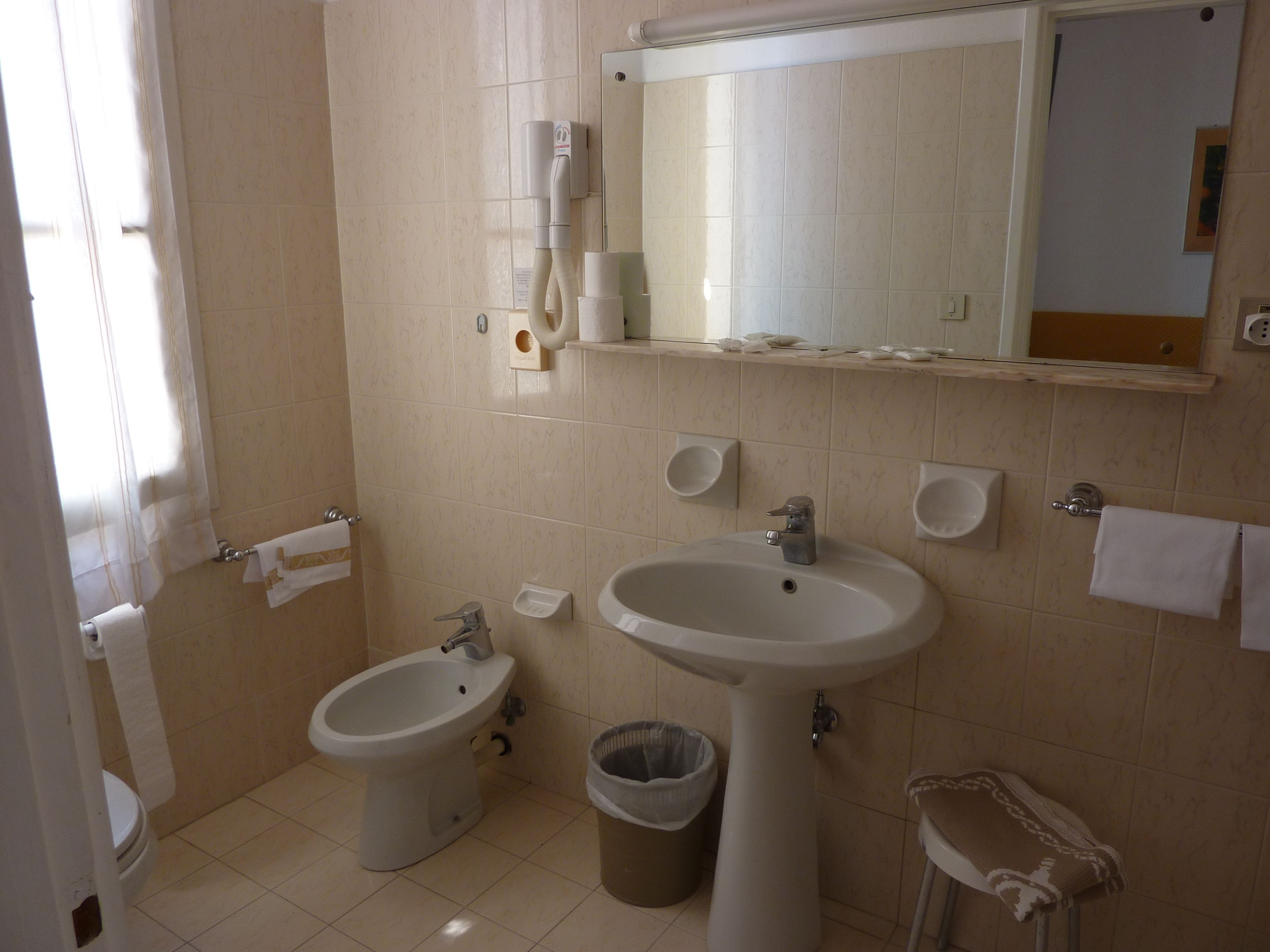 Un baño con bidé, lavamanos, espejo y cubo de basura.