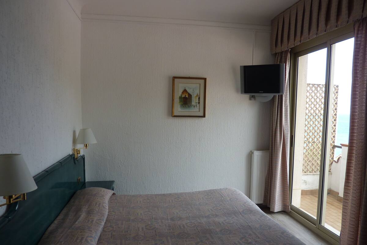 Een hotelkamer met een bed, een aan de muur bevestigde televisie en een raam met gordijnen.