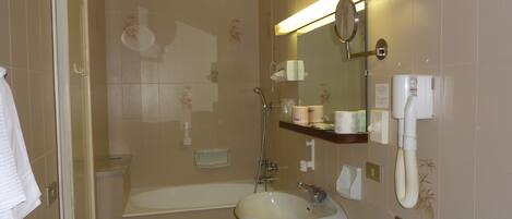 Een badkamer met een badkuip, wastafel en spiegel. Er staan toiletartikelen aan de muur en een handdoekhouder.