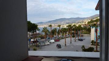 A parking lot with several cars and palm trees, a view of a city and mountains in the background, and a building with a blue and white facade.