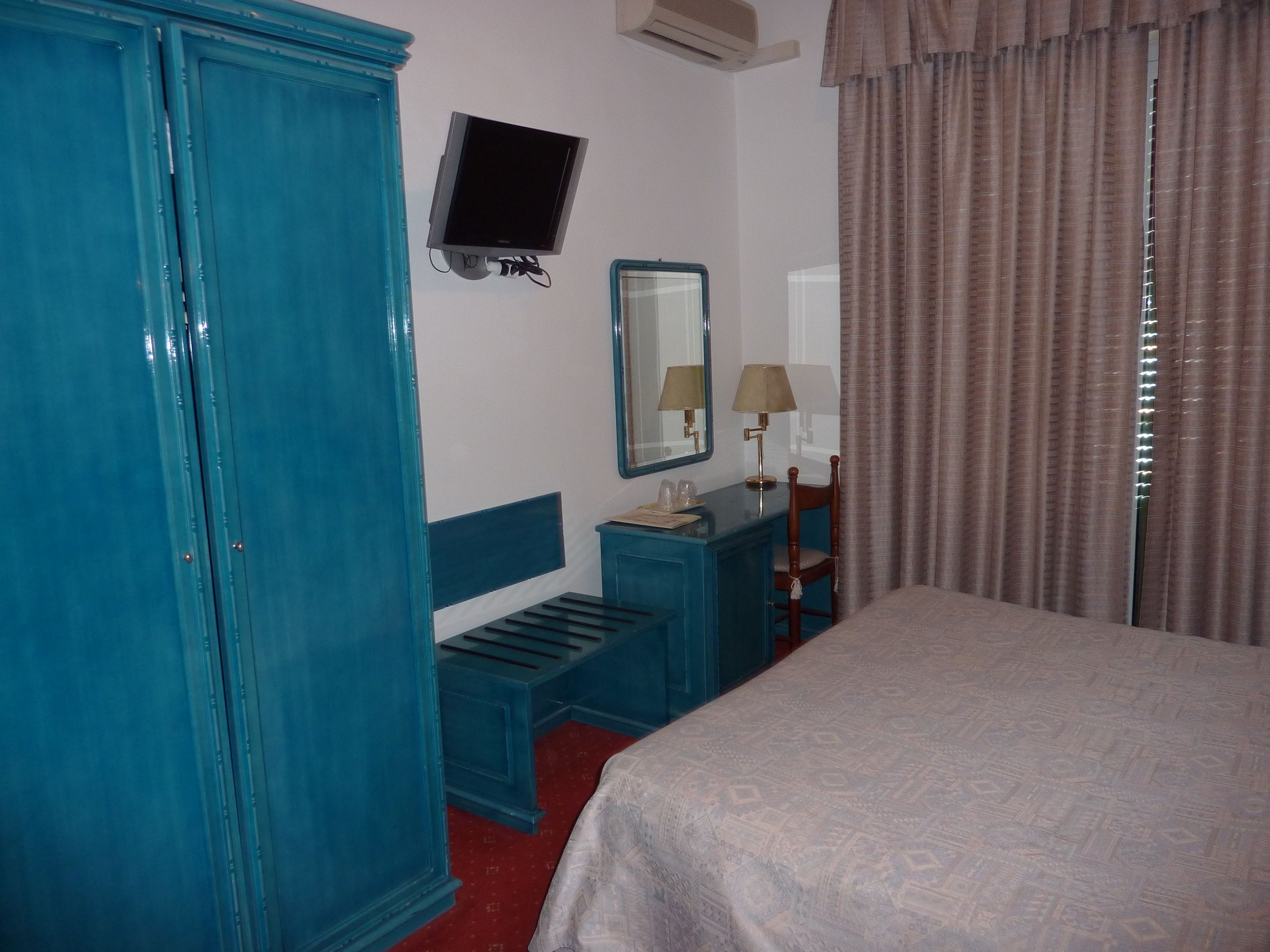 Habitación de hotel con una cama, un escritorio con silla, un televisor montado en la pared y un armario.