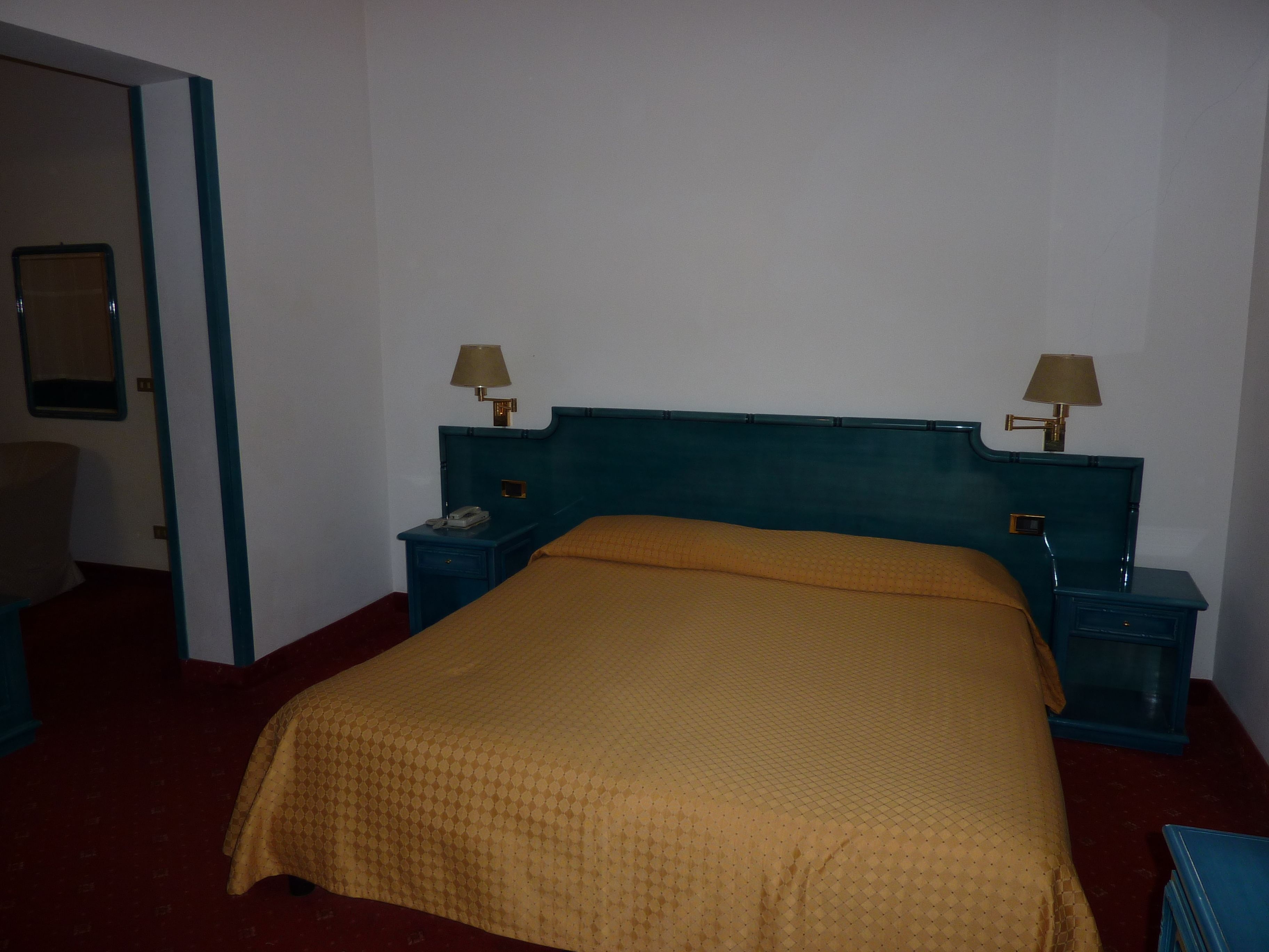 A single bed with a headboard, two bedside tables with lamps, a telephone, and a mirror on the wall.