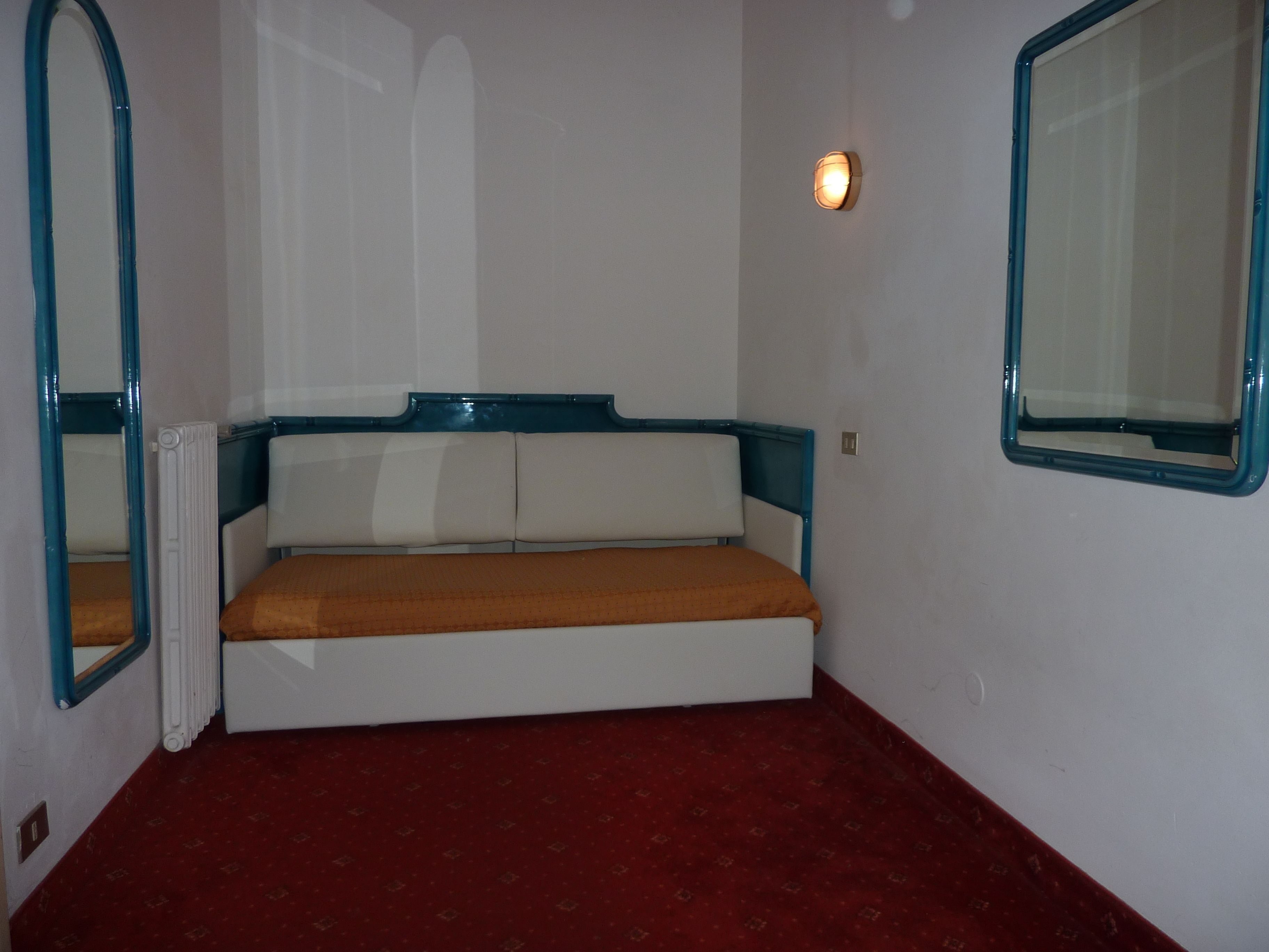 A small, single-bed room with a red carpet, white walls, and a blue-framed headboard.